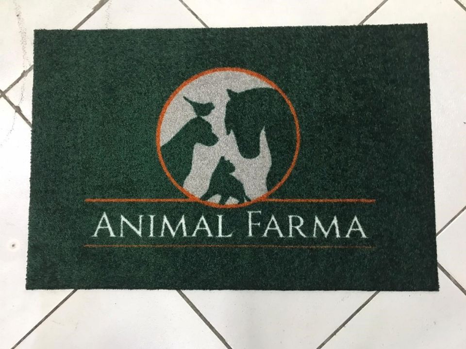 Tapete verde escuro personalizado com a logomarca Animal Farma, círculo prateado com silhuetas de animais em contorno laranja, textura de alta retenção de sujeira sobre piso de cerâmica clara, fotografia realista de tapete profissional para clínica veterinária