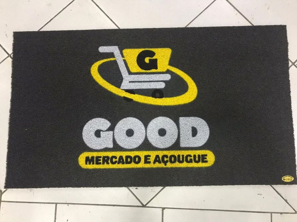 Capacho preto personalizado com a logomarca Good Mercado e Açougue em amarelo, branco e preto, ícone de carrinho de compras, impressão fiel de cores sobre fibra resistente, fotografia realista de tapete de identidade visual comercial